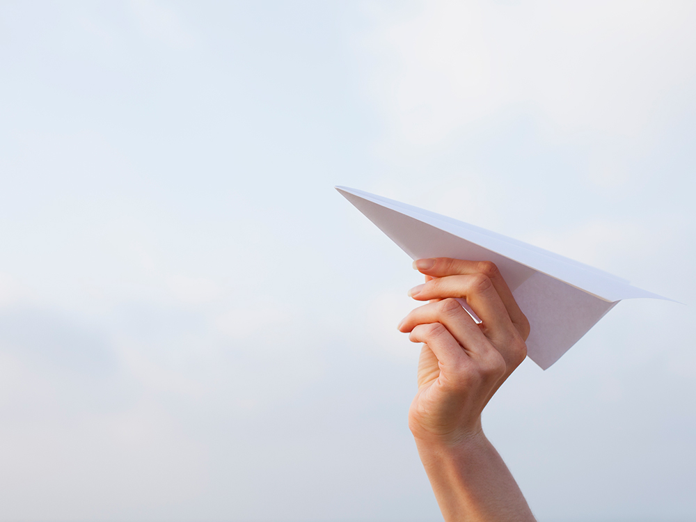 Hand holding a paper airplane ready to launch into the sky