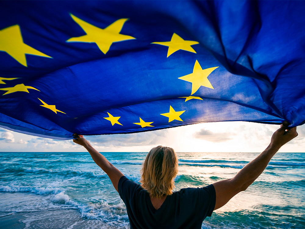 Man holding EU European Union flag waving in front of Mediterranean sunrise seascape