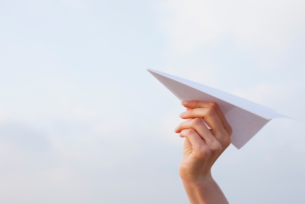 Hand holding a paper airplane ready to launch into the sky
